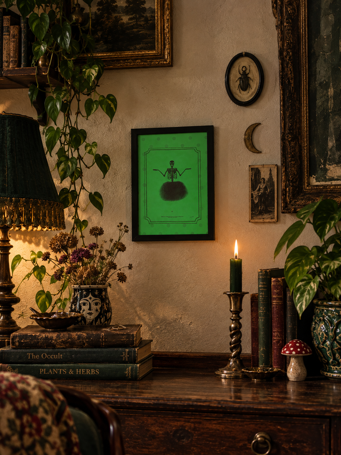 A framed art print featuring a green background with a black silhouette illustration of a skeleton key, displayed on a rustic wall in a cozy, vintage-style room with a lamp, candle, books, and plants.